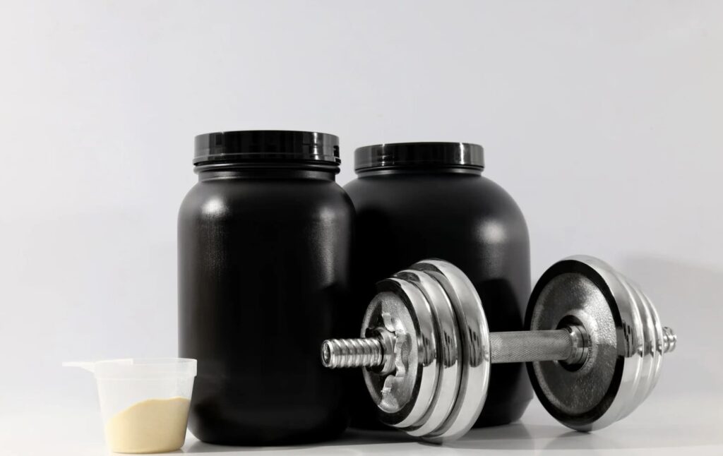 Suplementación deportiva. Aparece una mancuerna con dos botes de proteínas
