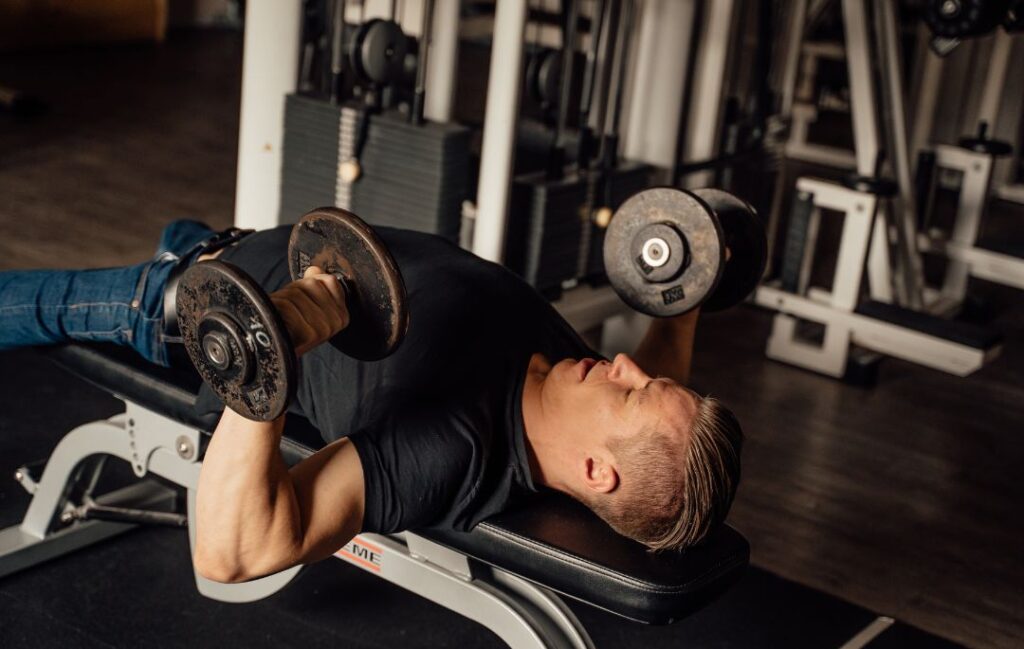 un hombre realizando press de banca con mancuernas